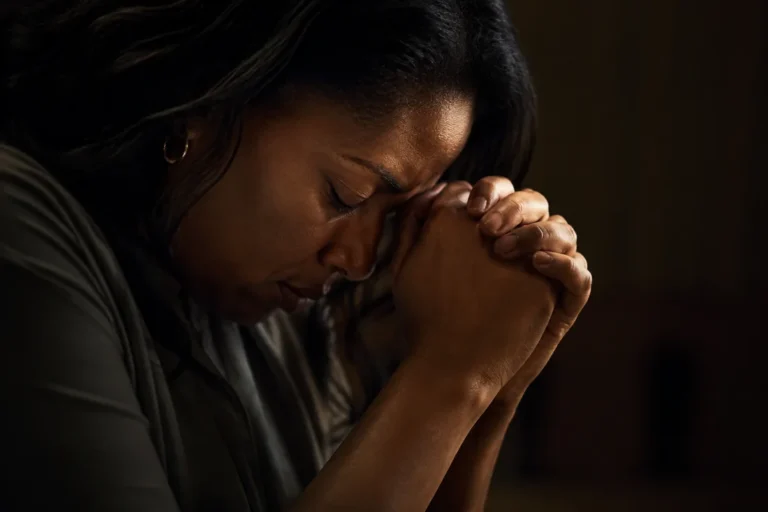 A person praying with head bowed and hands clasped together